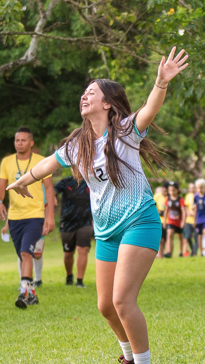 Menina comemorando de braços abertos em campo no Acampa GoTo